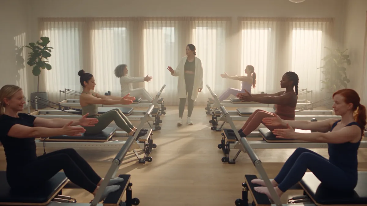 A full reformer class in a bright studio, the owner teaching at the front.