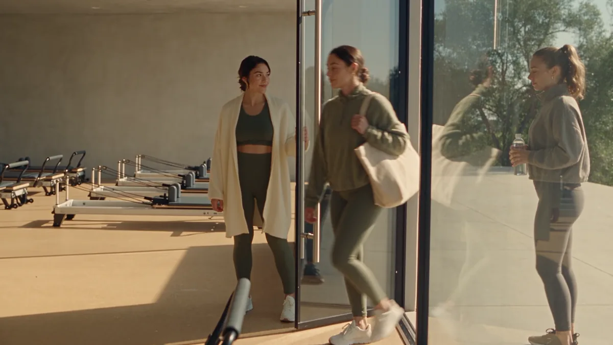 The owner holds the glass door open as two women arrive for class.